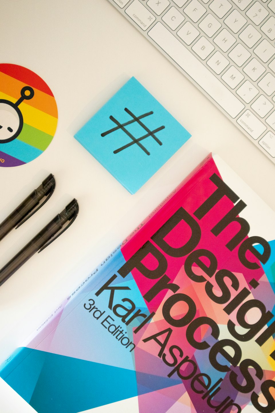 Creative workspace flat lay with keyboard, pens, and book.