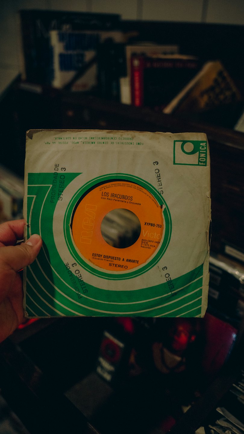 Hand holds a vintage vinyl record in its worn sleeve.