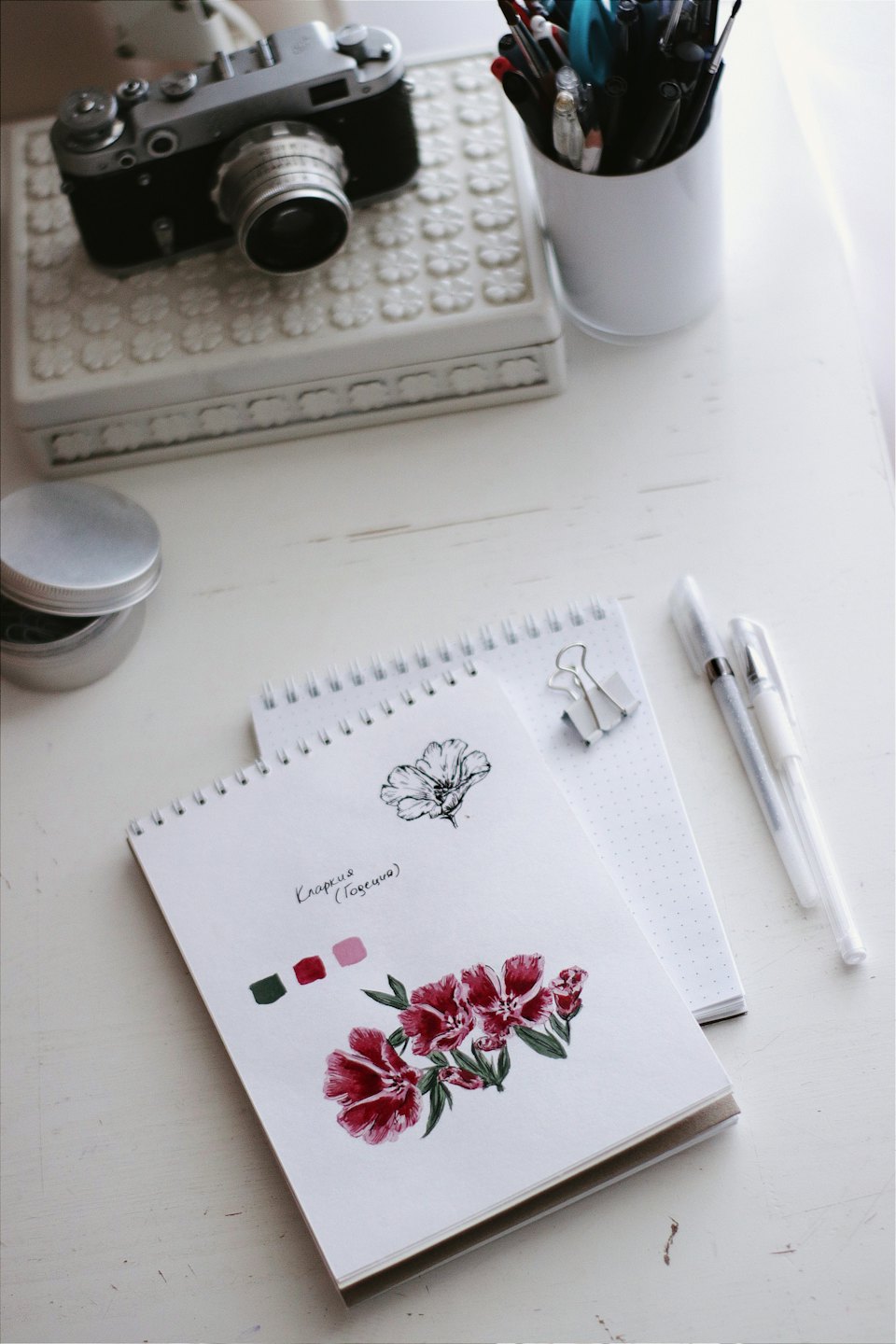 Art supplies and illustrated notebooks sit on a wooden desk.